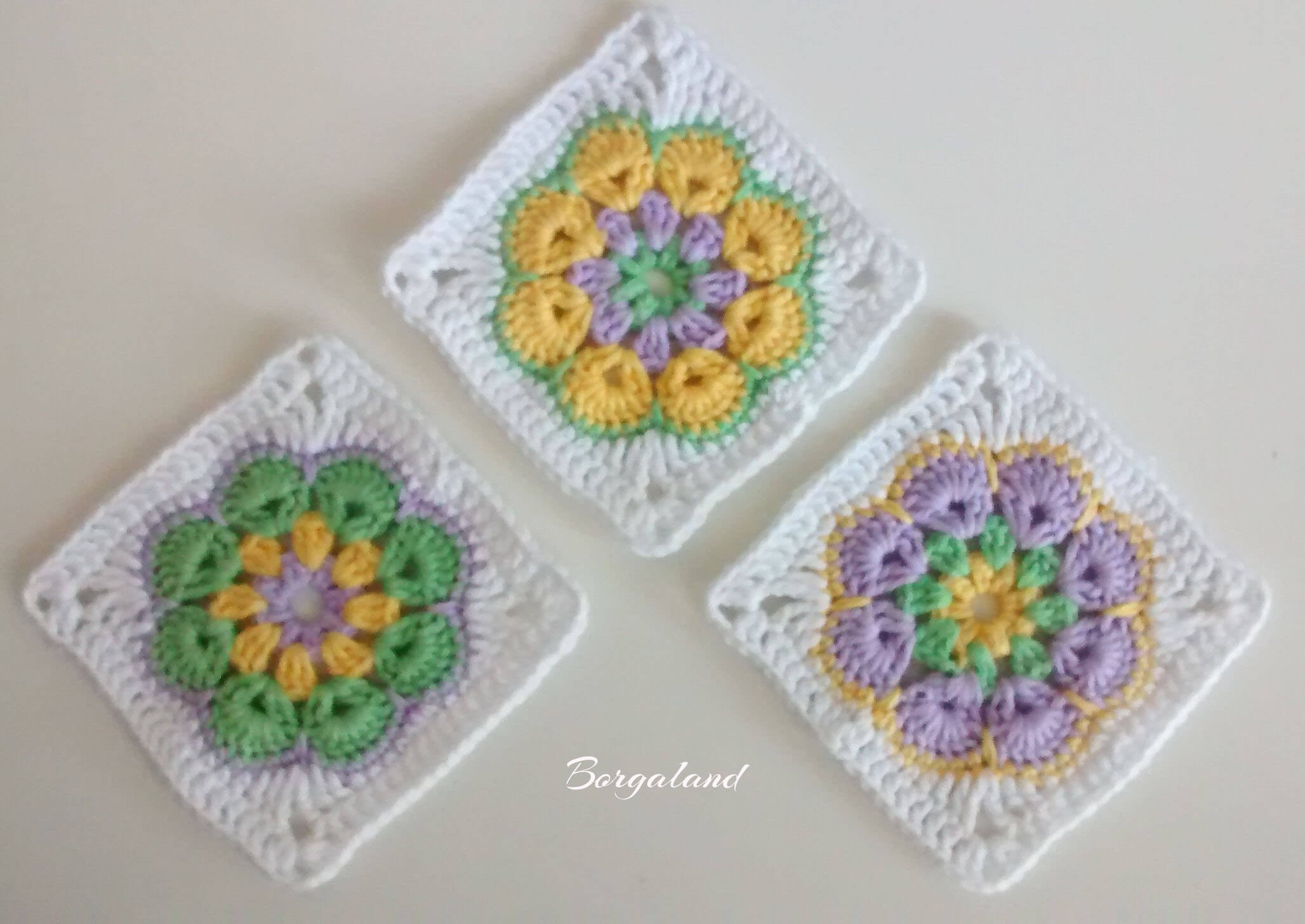 Zwei gehäkelte African Flower Granny Squares mit bunter Blume in der Mitte und weißem Rand – auf hellem Hintergrund