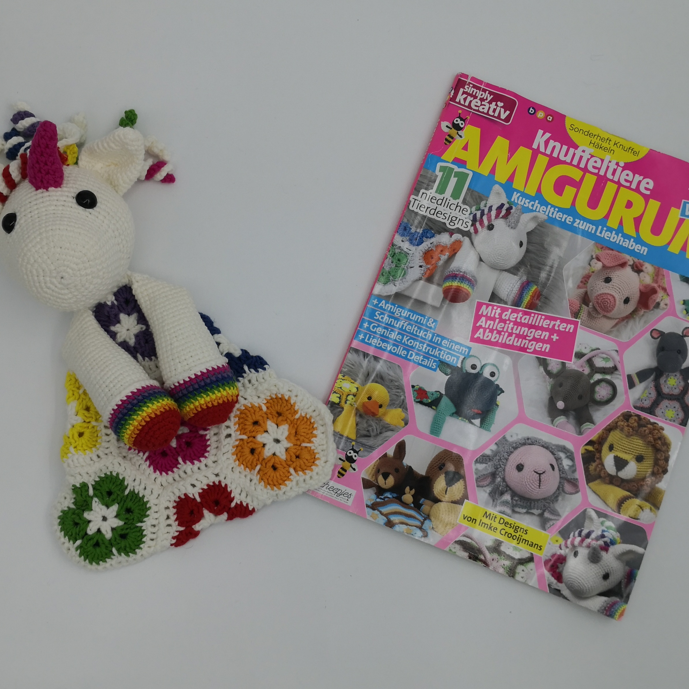 Amigurumi-Einhorn mit bunter Granny-Decke und Zeitschrift über Häkeltiere – farbenfrohe Inspiration für Häkelprojekte
