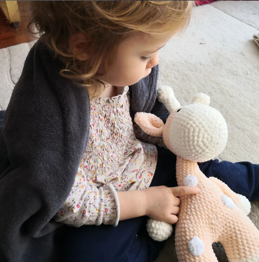 Kleines Kind spielt mit einer großen gehäkelten Giraffe aus Plüschgarn – DIY Kuscheltier