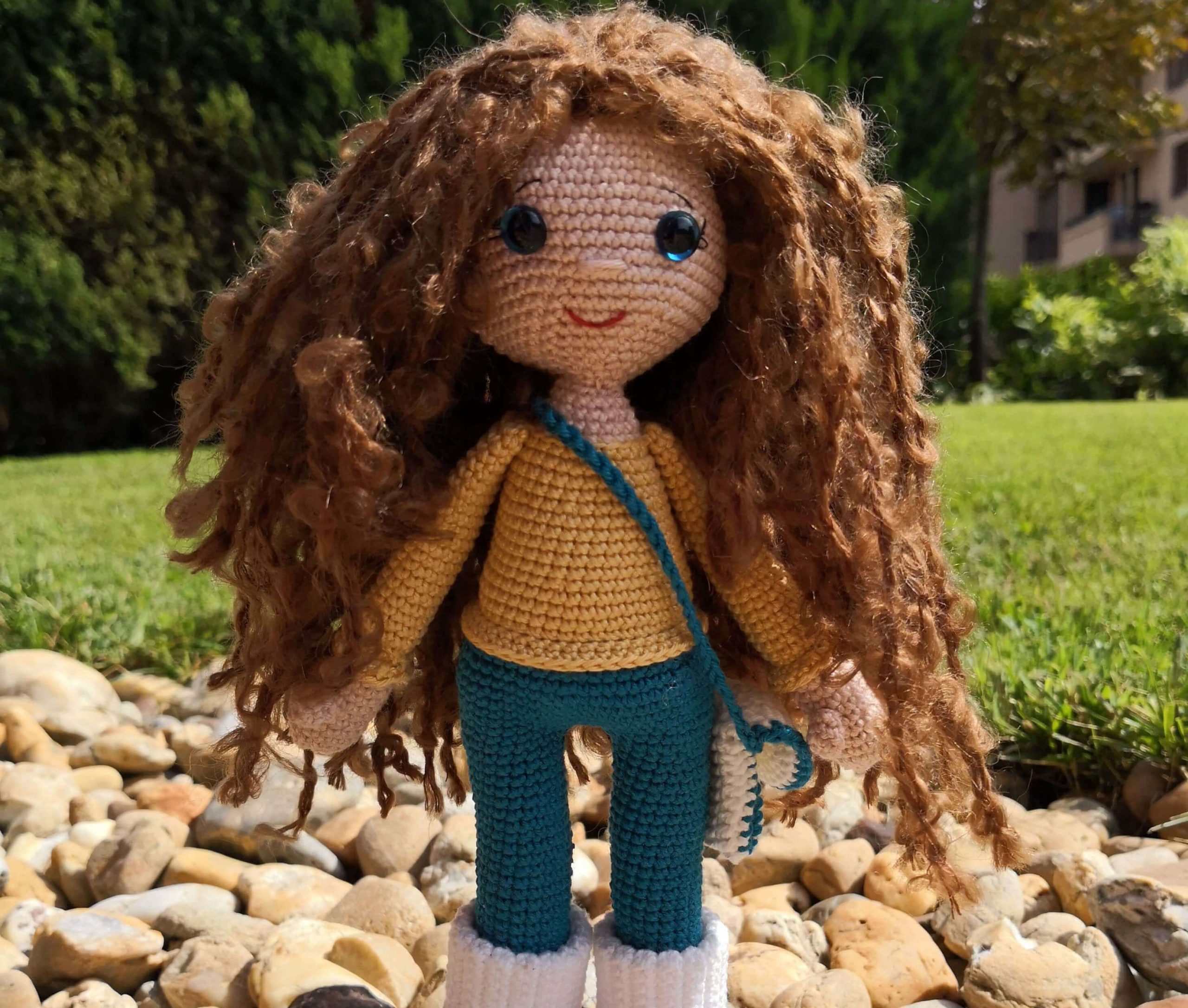 Gehäkelte Amigurumi-Puppe mit lockigem Haar, Jeans, gelbem Pullover und Umhängetasche – draußen auf Steinweg fotografiert