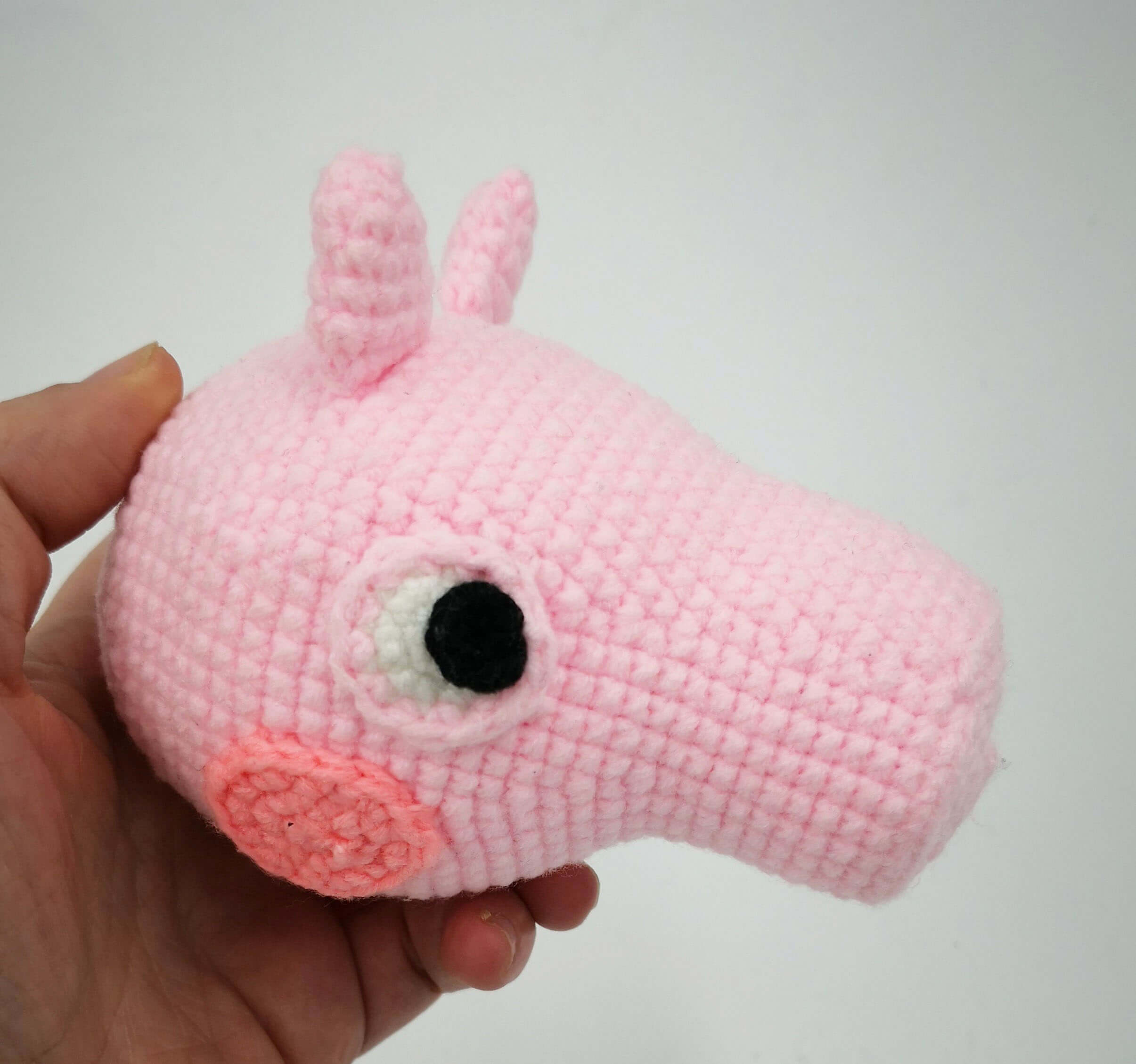 Gehäkelter Peppa-Wutz-Kopf in Rosa, in der Hand gehalten – Amigurumi-Projekt