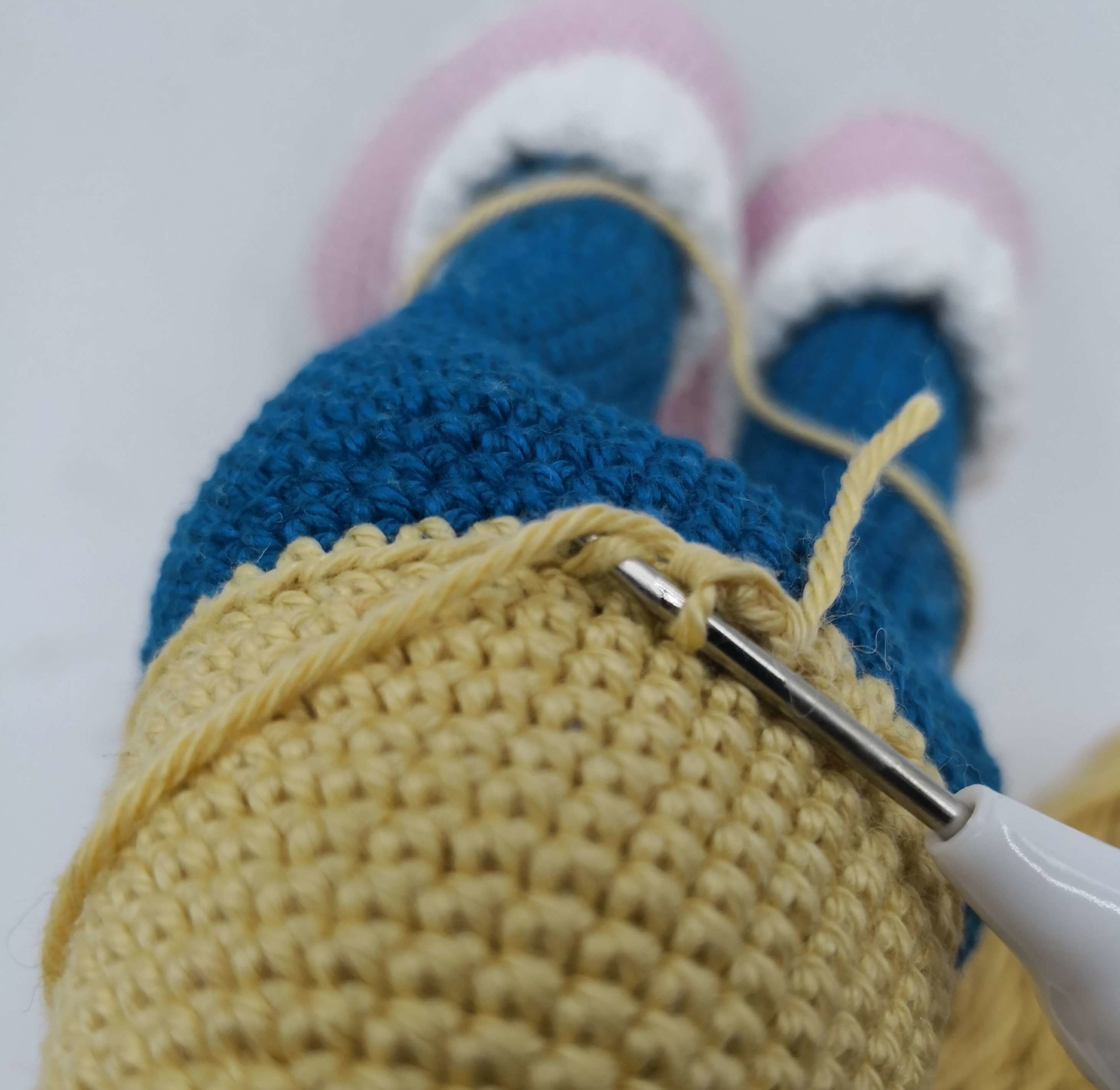 Rückansicht einer gehäkelten Amigurumi-Puppe mit bestickter Tasche, Jeans und weißen Stiefeln