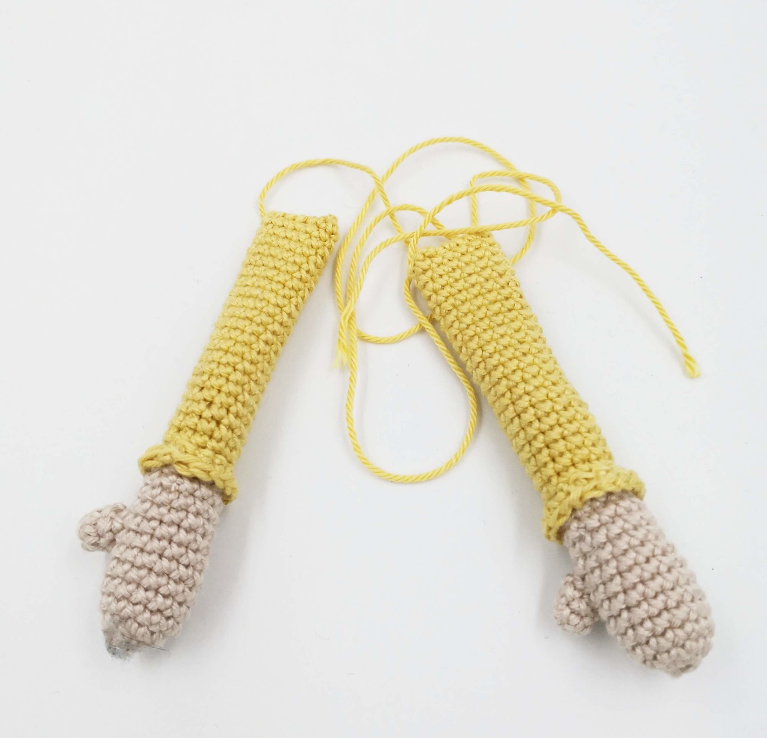 Zwei gehäkelte Amigurumi-Arme mit gelbem Pulloverärmel und grauen Händen – bereit zum Annähen