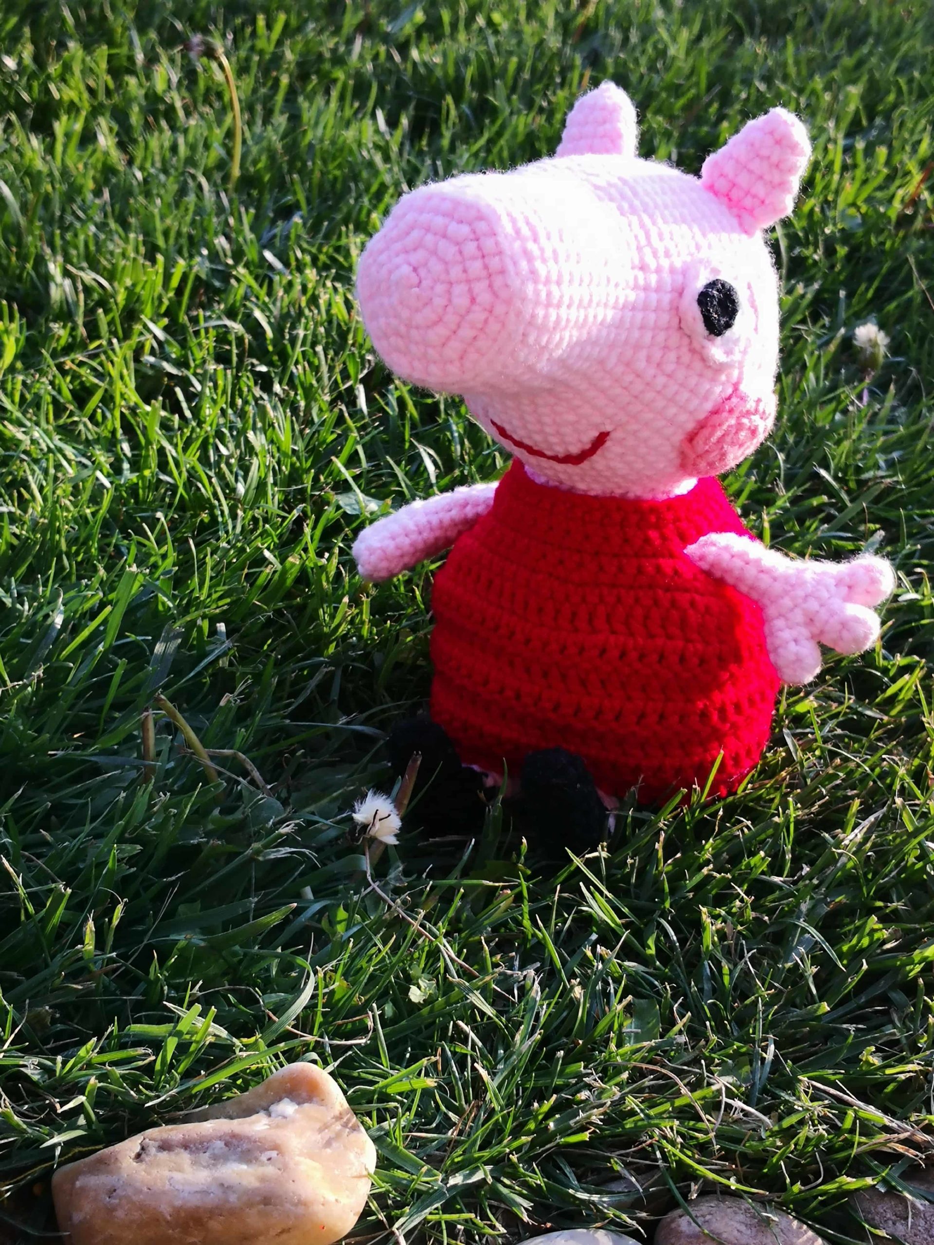 Fertige gehäkelte Peppa-Wutz-Figur sitzt im Gras – handgemachtes Amigurumi-Spielzeug
