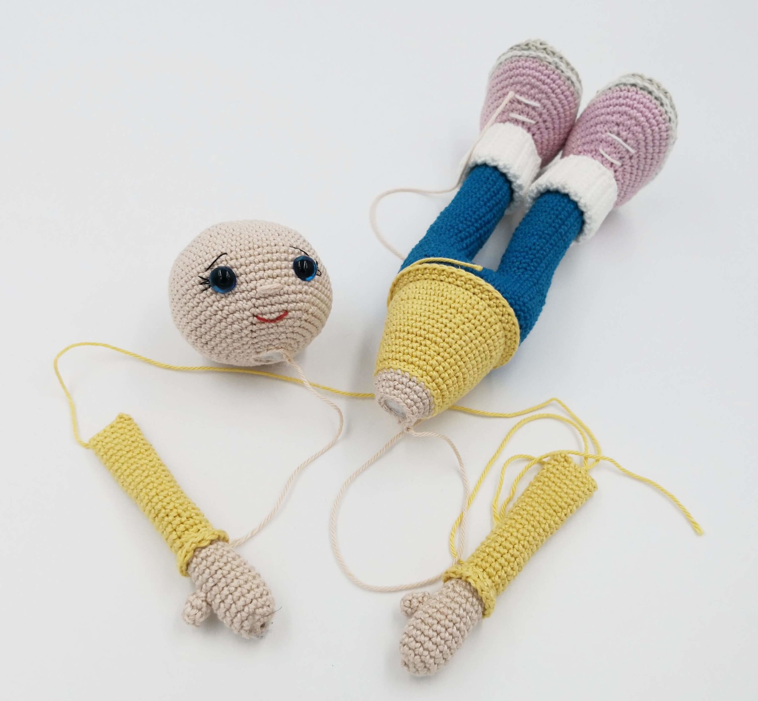 Einzelne gehäkelte Teile einer Amigurumi-Puppe – Kopf, Arme und Beine vor dem Zusammennähen