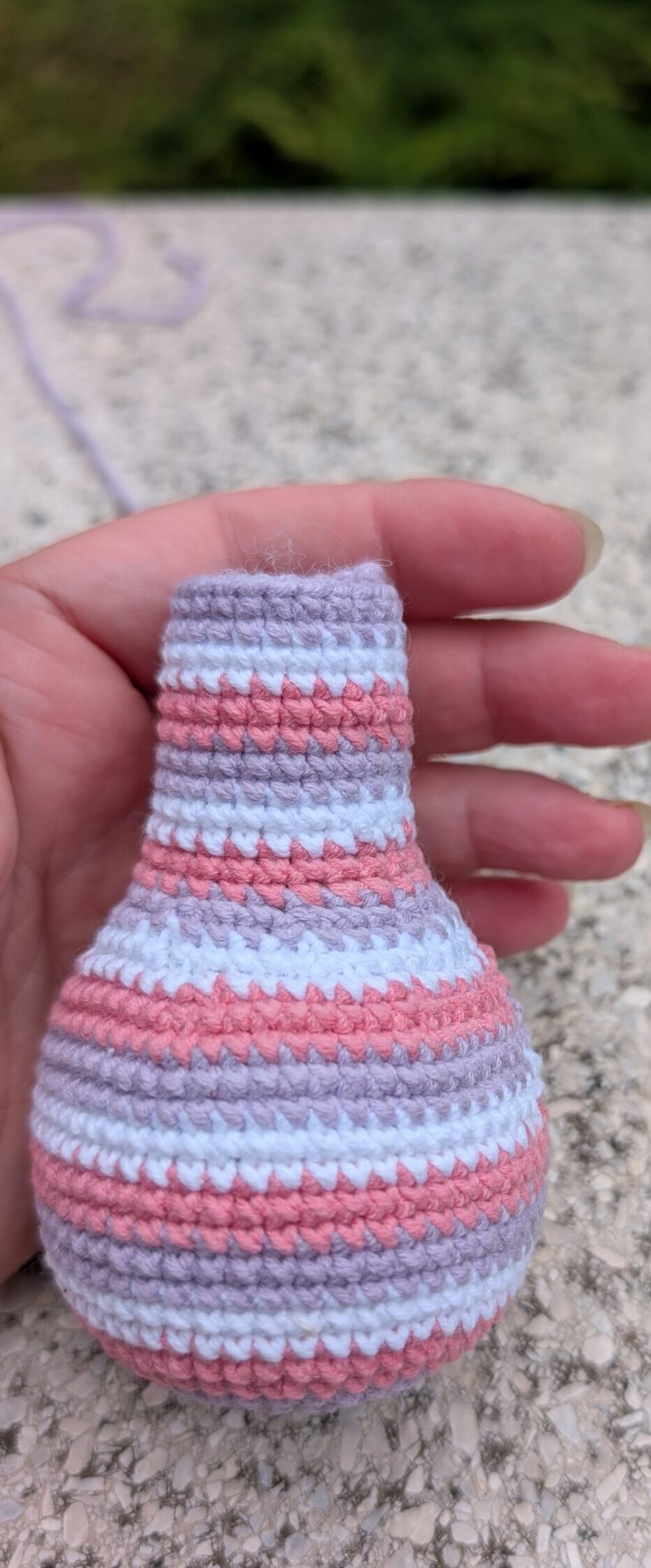 Gehäkelte Rückansicht einer gestreiften Amigurumi-Giraffe in Rosa, Lila und Weiß.
