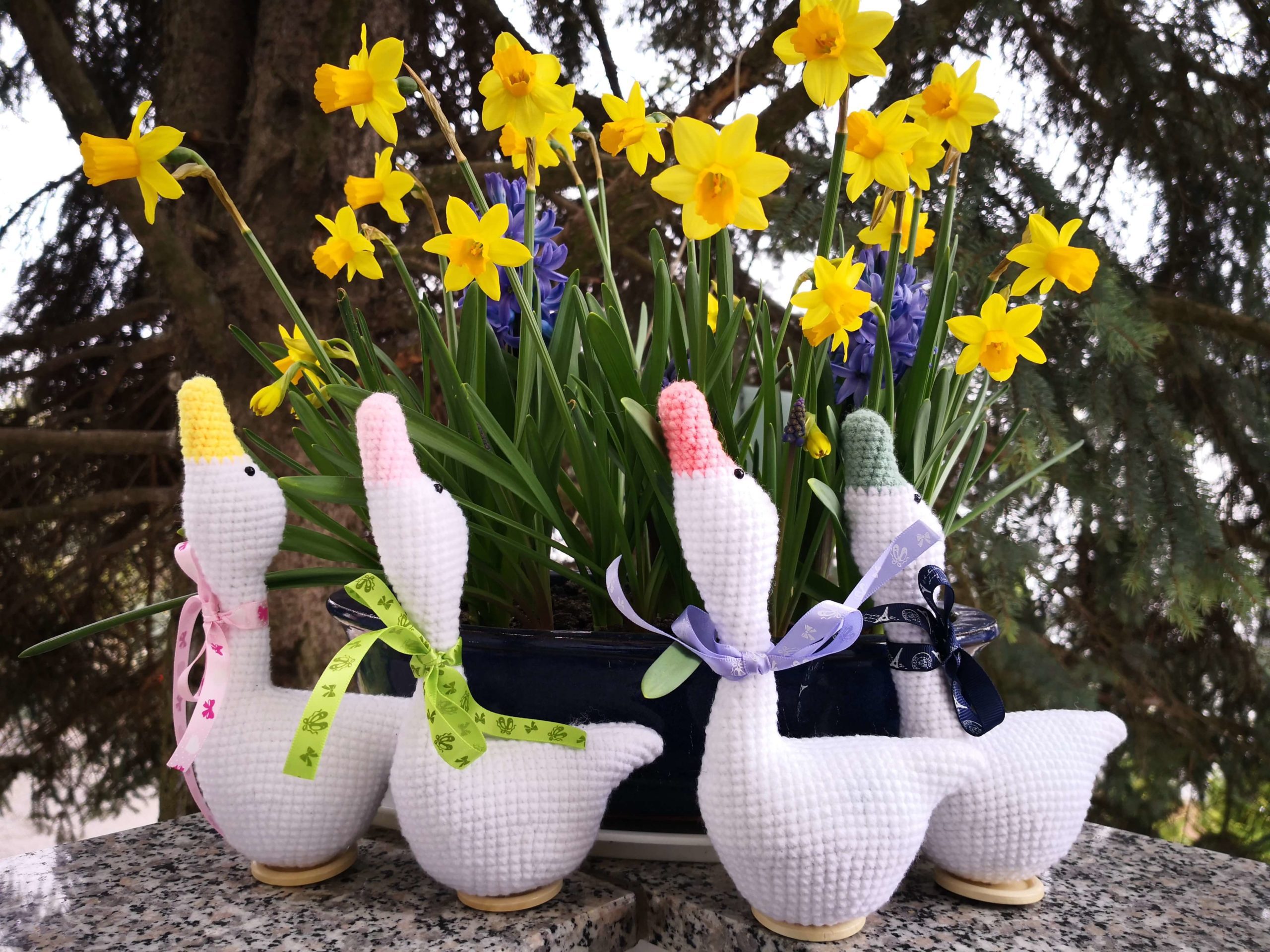 Häkelfiguren in Form von weißen Osterhasen vor gelben Tulpen – ein saisonales Projekt für Anfänger beim Häkeln lernen.