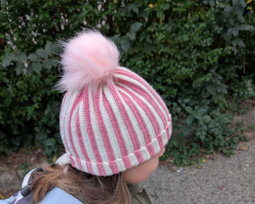 Mädchen mit gehäkelter Mütze im Rippenmuster, Rosa-Weiß mit Bommel