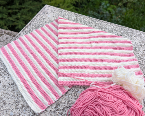 Rosa-weiße Häkelarbeit im Rippenmuster mit Garn und Häkelnadel